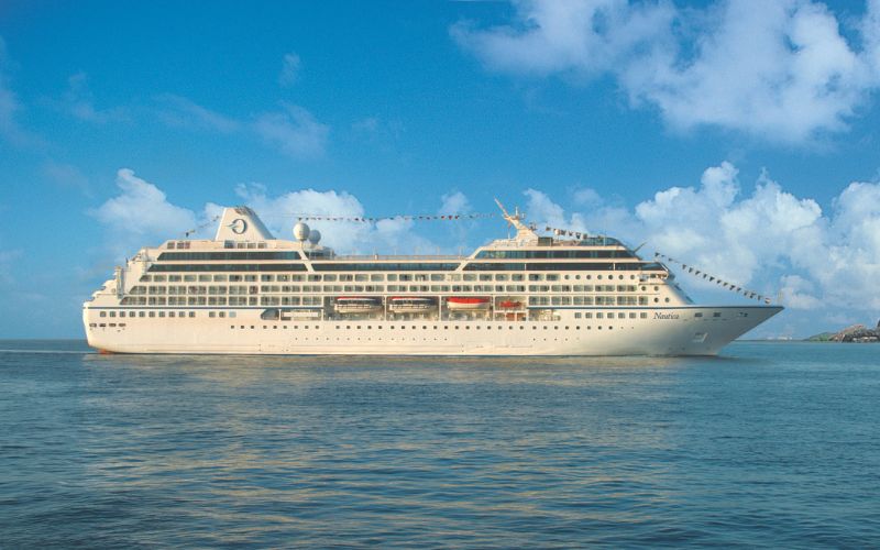 A side angle shot of the Oceania Nautica calmly floating on the ocean with a clear sky backdrop