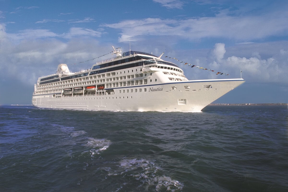 A white Oceania Cruises ship sailing on the ocean under a partly cloudy blue sky.