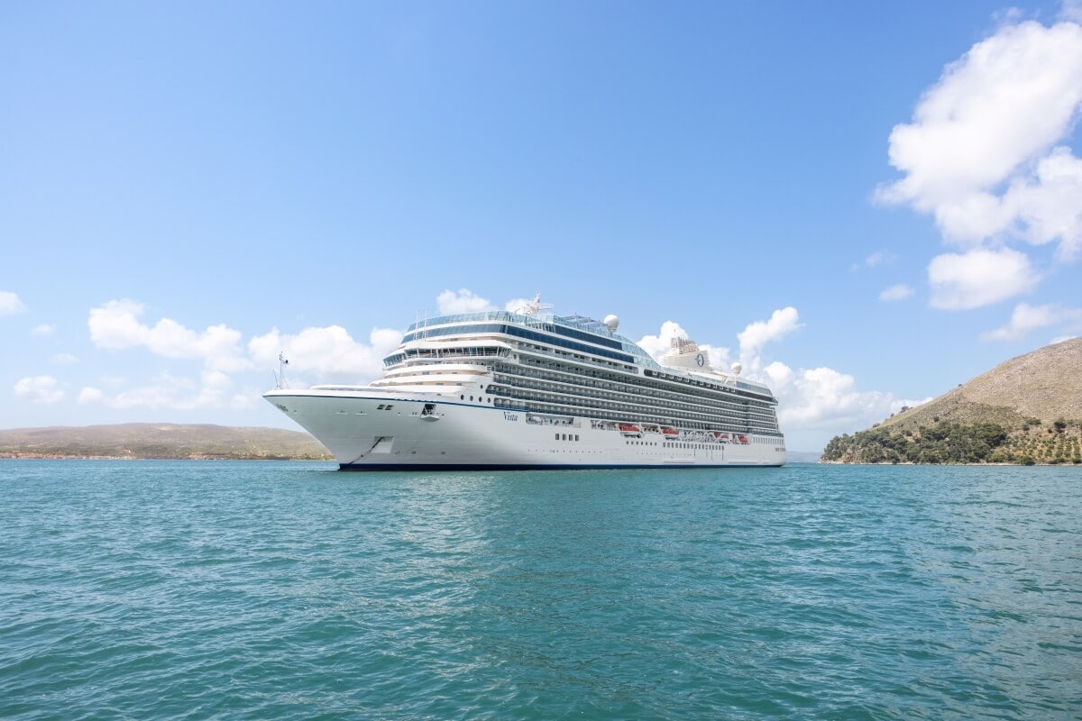 A large cruise ship from Oceania Cruises anchored near a hilly coastline under a clear blue sky.