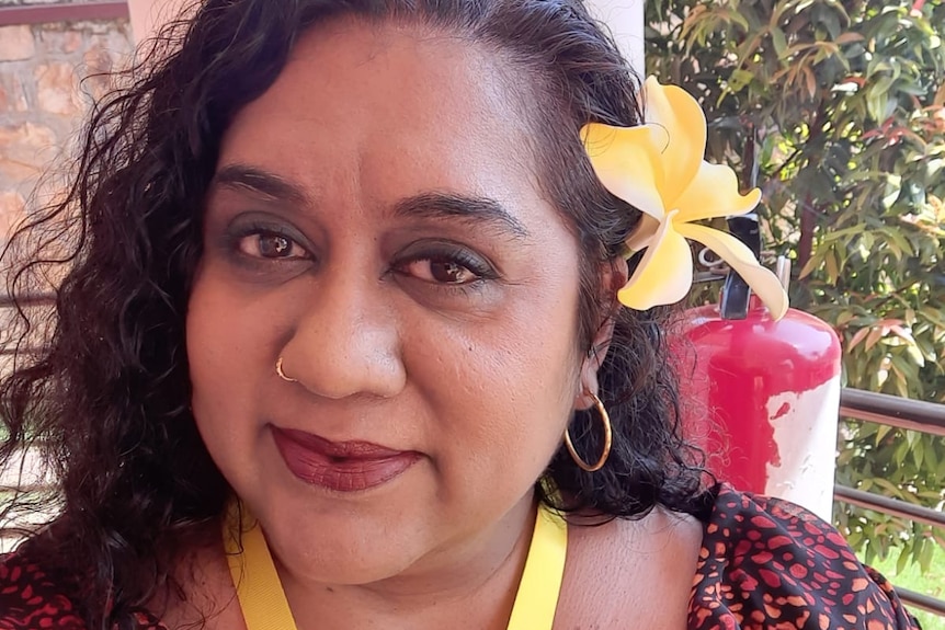 A selfie of a woman with dark hair and a flower in her ear