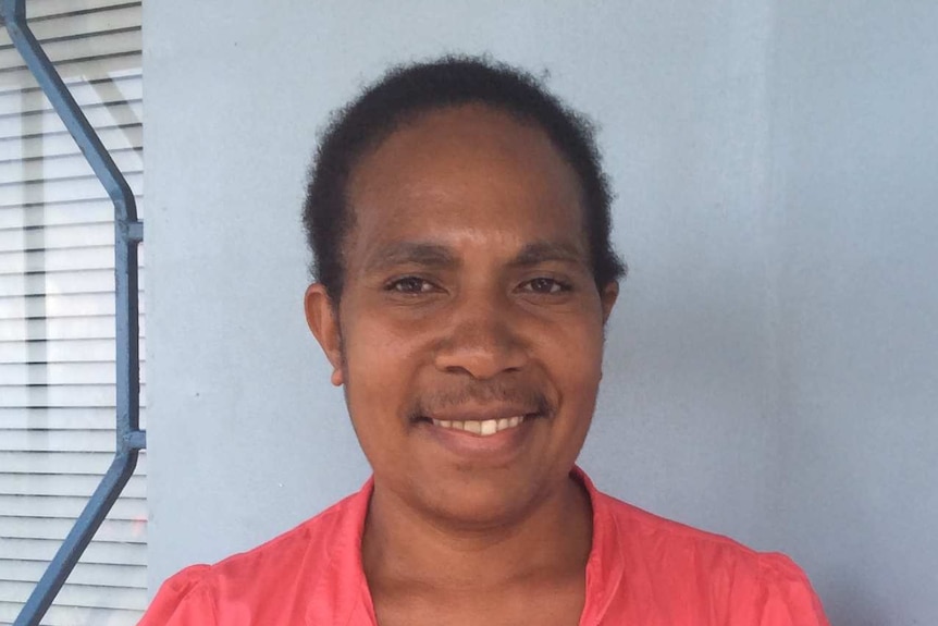 Headshot of PNG woman, hair pulled back, wears pink top and smiles. 