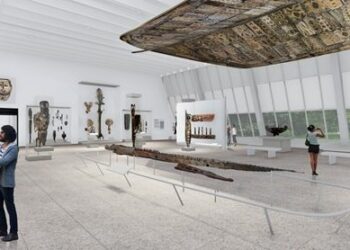 A gallery space with a large wooden ceiling hanging overhead. Guests engage with one another inside the gallery